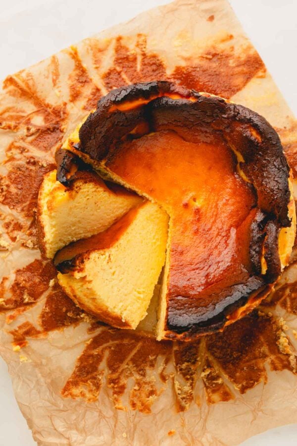 A whole basque cheesecake on a baking paper with 2 slices cut.