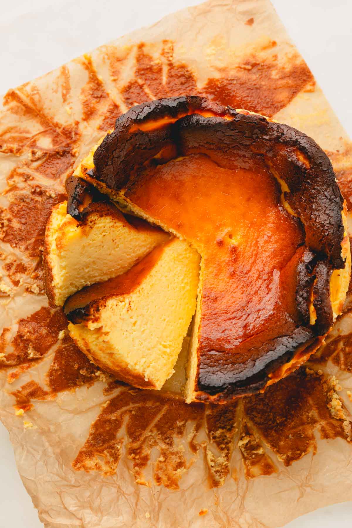 A whole basque cheesecake on a baking paper with 2 slices cut.