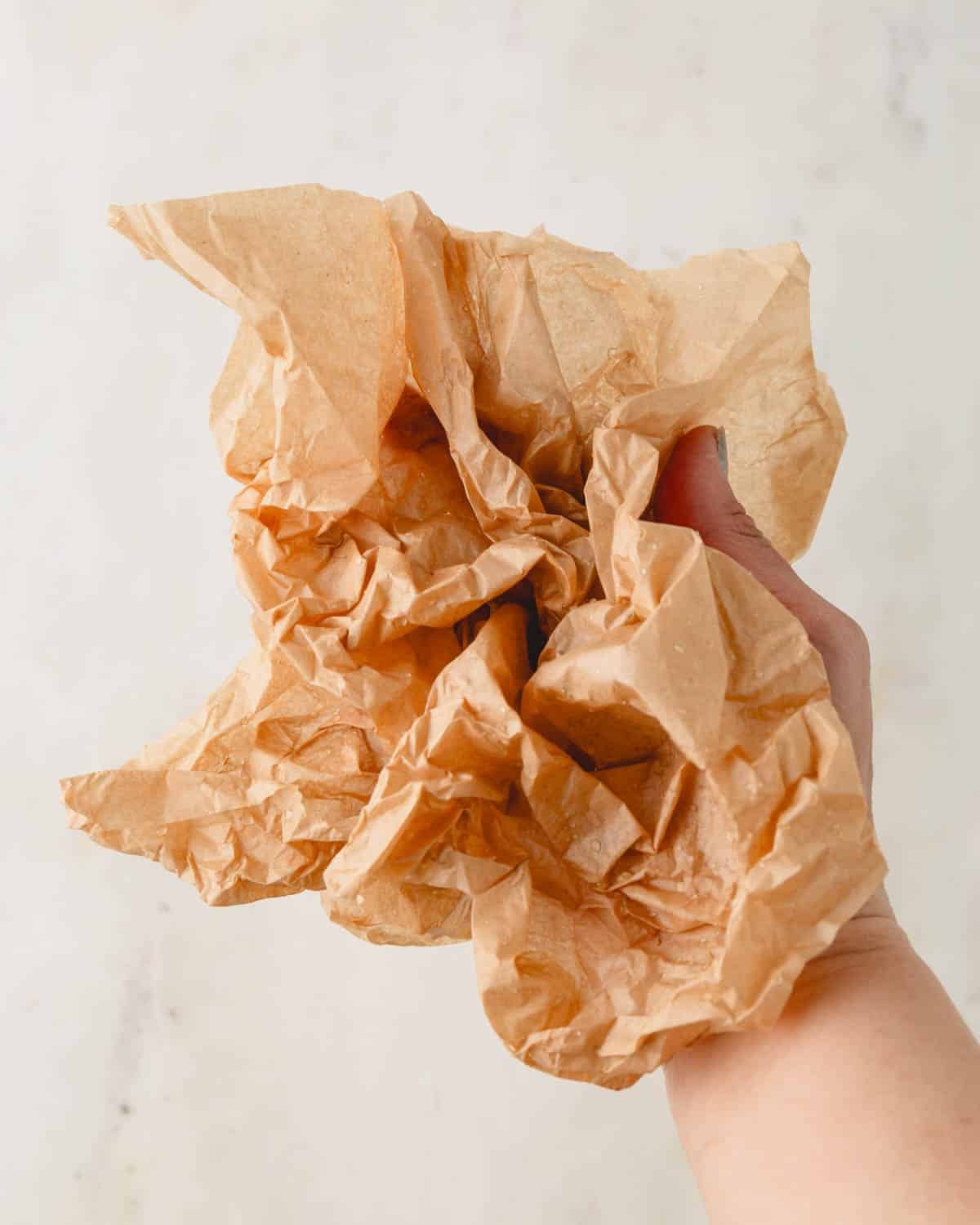 Damp wrinkled brown parchment paper crumbled in a hand.